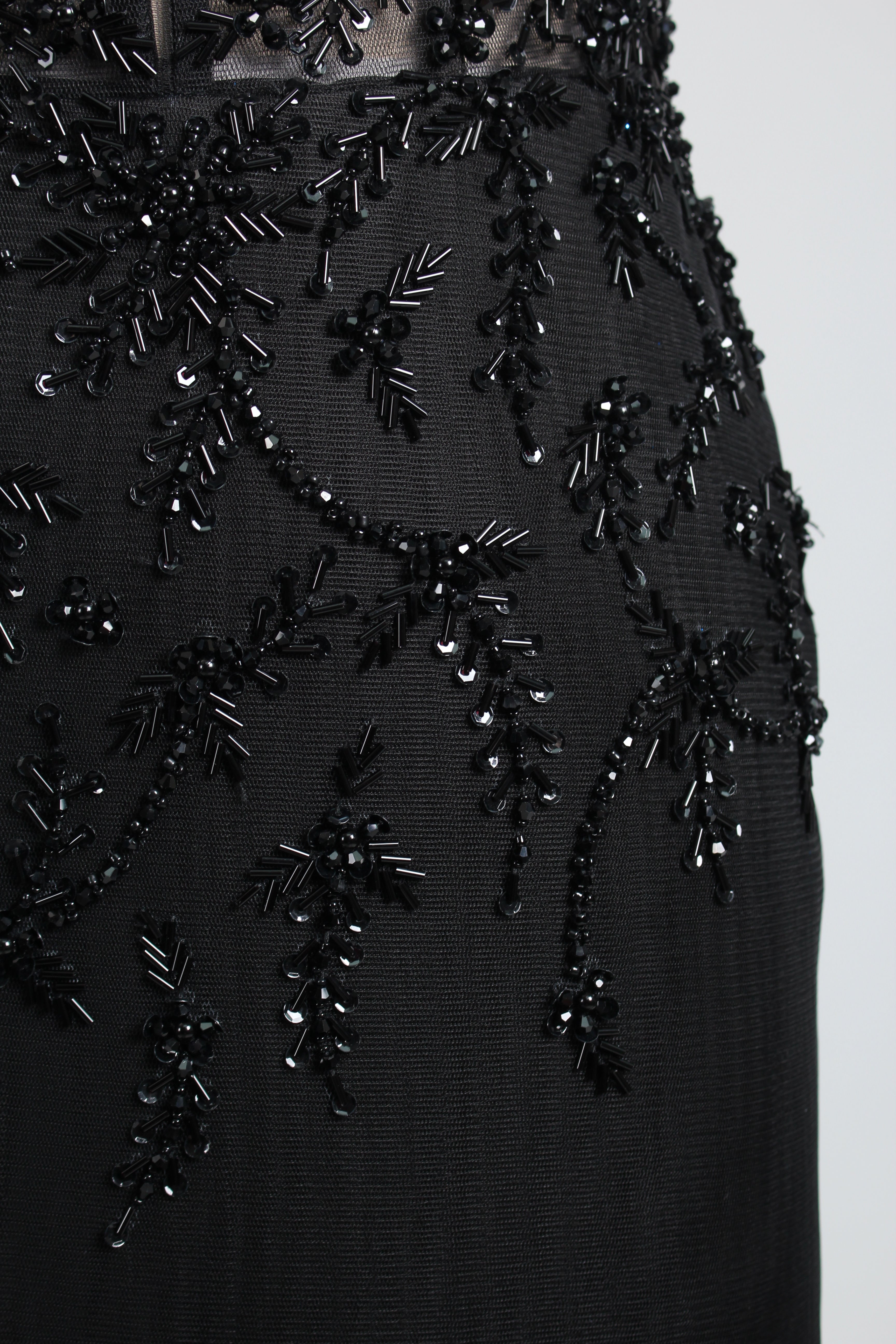 A mannequin displays a black mermaid - style gown. It has thin straps, a deep V - neckline with sheer panels, and intricate black bead embroidery. The layered tulle skirt adds a romantic touch, perfect for formal events like galas or weddings, exuding elegance and sophistication.7