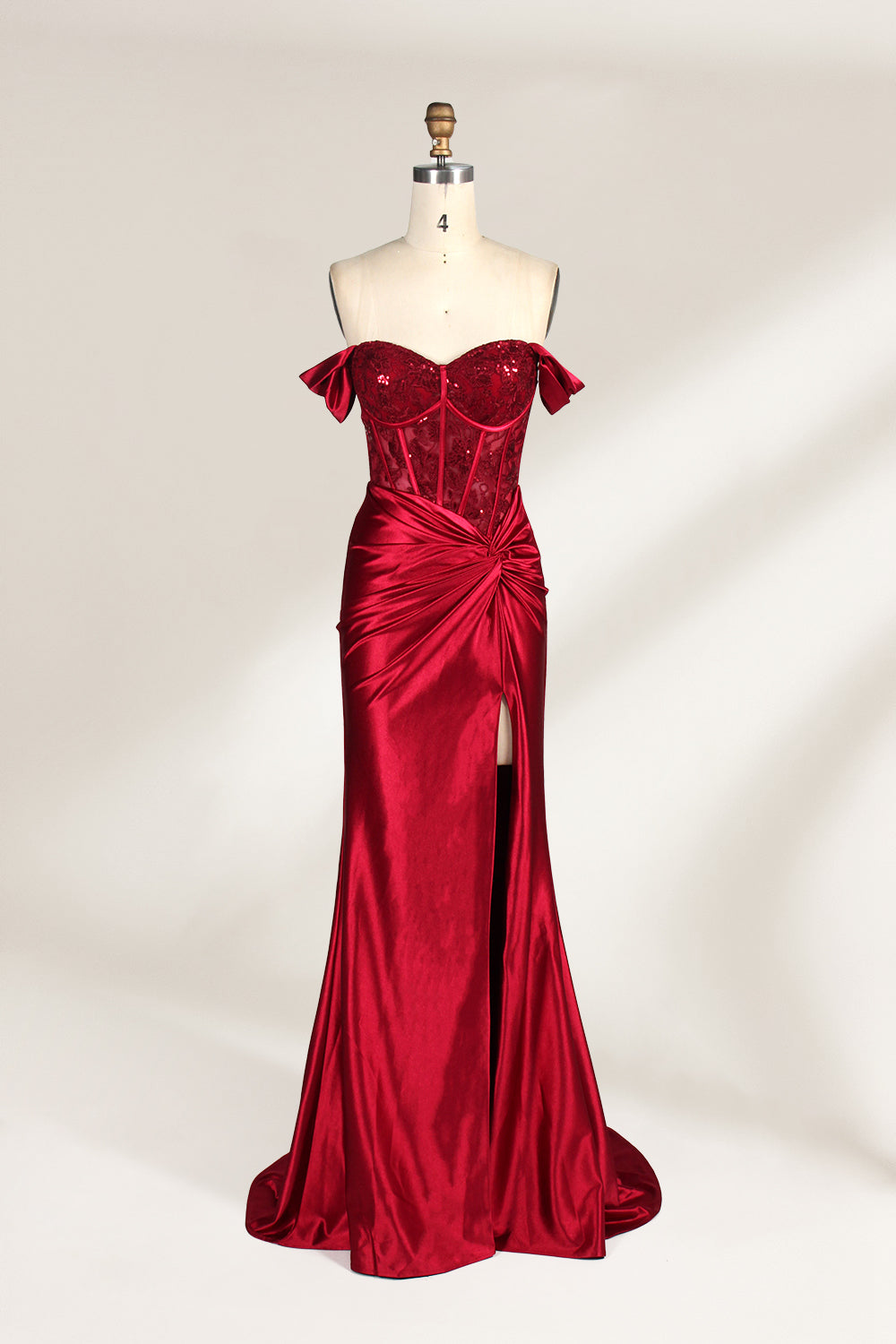 Against a light - hued backdrop, a mannequin displays a strapless red satin gown. It boasts off - shoulder ruffled sleeves, a lace - detailed bodice, and a high side slit. The ruched satin skirt and sequin - adorned top exude charm, suitable for formal dinners or galas.1