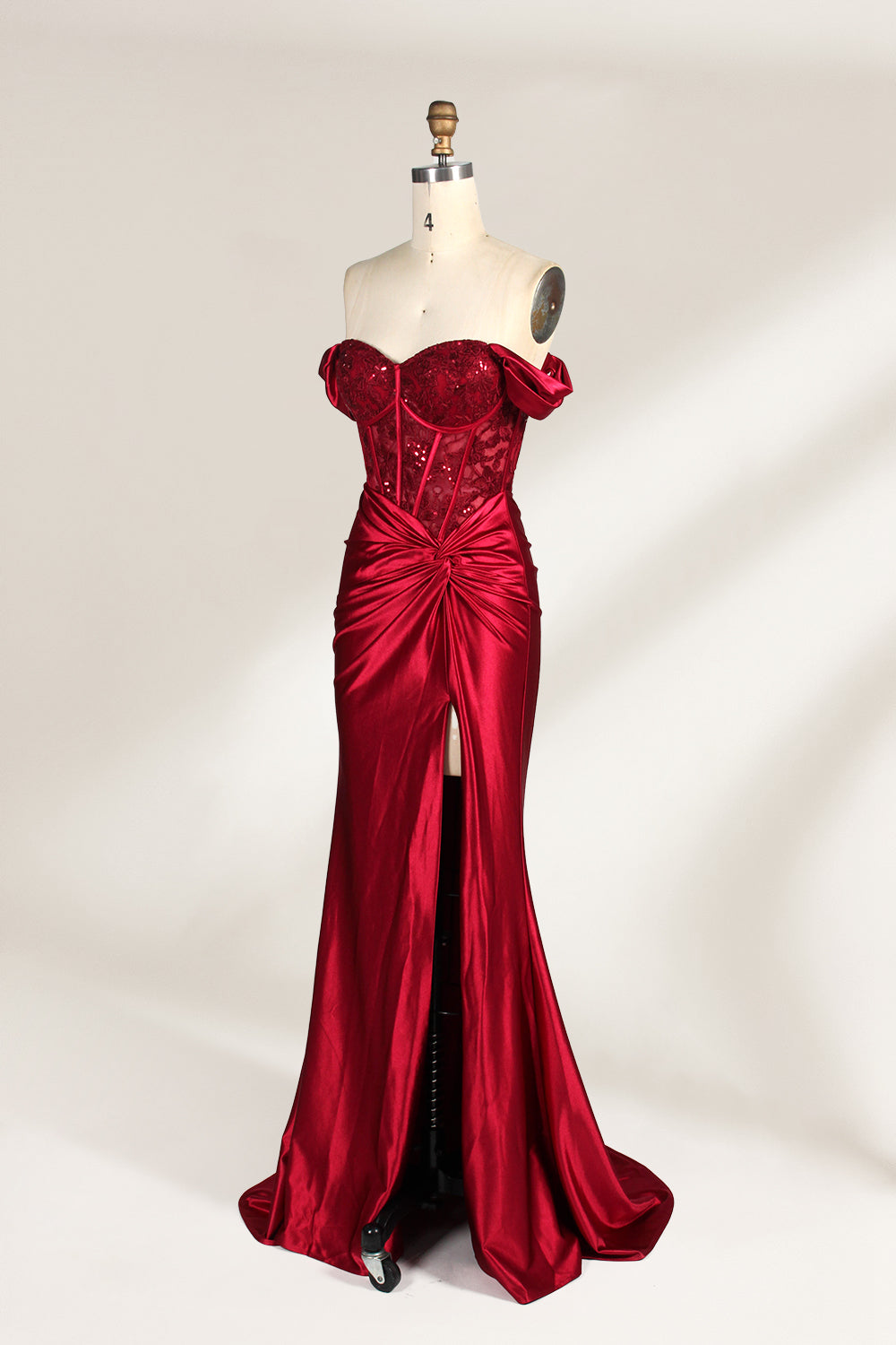 Against a light - hued backdrop, a mannequin displays a strapless red satin gown. It boasts off - shoulder ruffled sleeves, a lace - detailed bodice, and a high side slit. The ruched satin skirt and sequin - adorned top exude charm, suitable for formal dinners or galas.6
