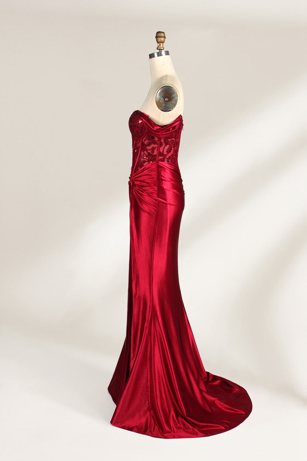 Against a light - hued backdrop, a mannequin displays a strapless red satin gown. It boasts off - shoulder ruffled sleeves, a lace - detailed bodice, and a high side slit. The ruched satin skirt and sequin - adorned top exude charm, suitable for formal dinners or galas.5
