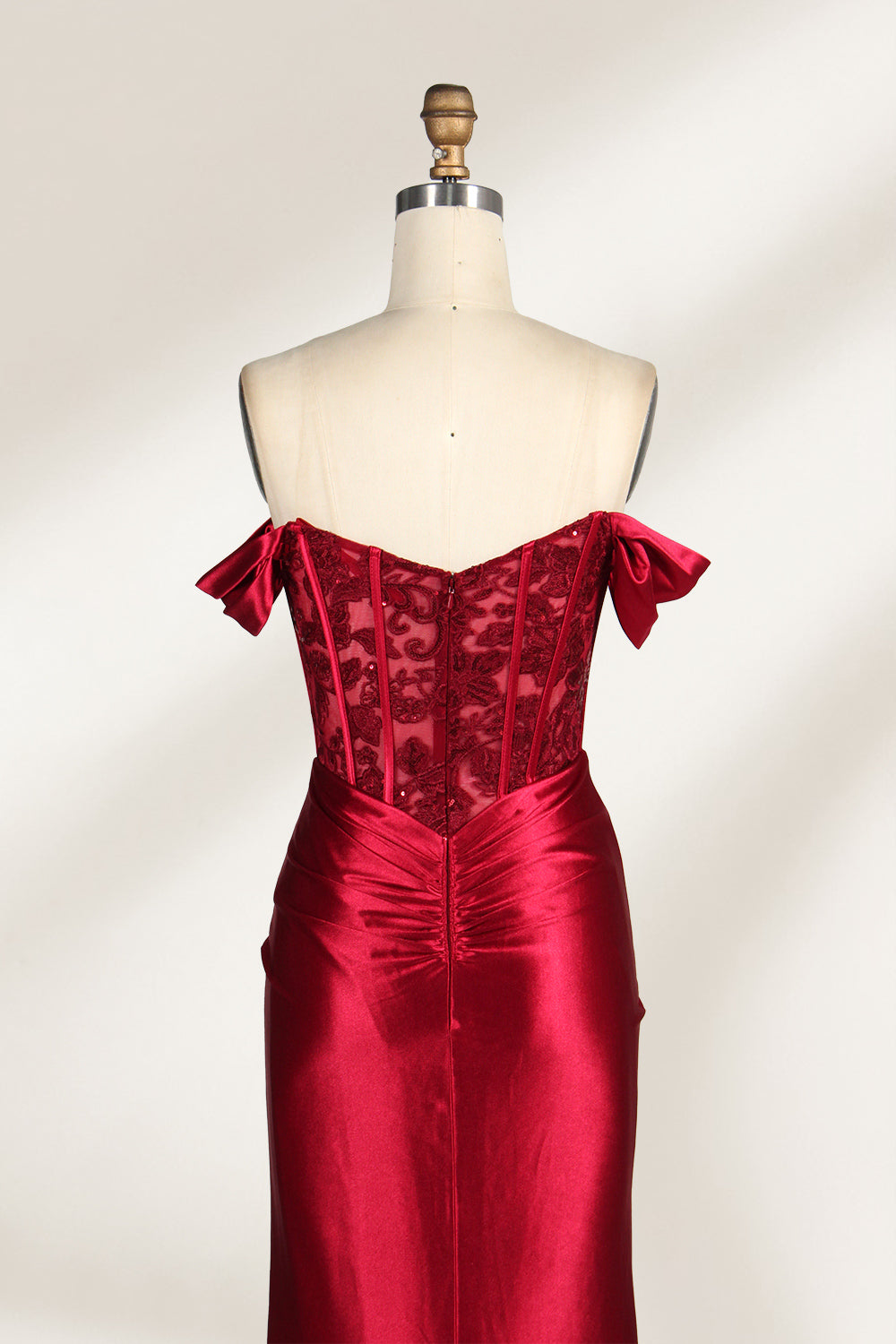 Against a light - hued backdrop, a mannequin displays a strapless red satin gown. It boasts off - shoulder ruffled sleeves, a lace - detailed bodice, and a high side slit. The ruched satin skirt and sequin - adorned top exude charm, suitable for formal dinners or galas.4