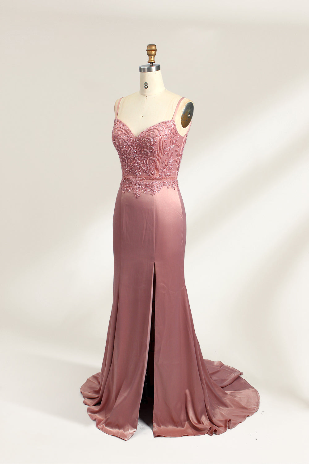 A photograph of a model mannequin wearing a floor-length, mauve satin gown with a deep V-neckline. The bodice is adorned with intricate lace detailing, featuring floral patterns and a subtle sheen. The gown has a thigh-high slit on the right side, adding a touch of elegance. The mannequin stands against a plain white background, highlighting the dress's smooth texture and elegant silhouette.03