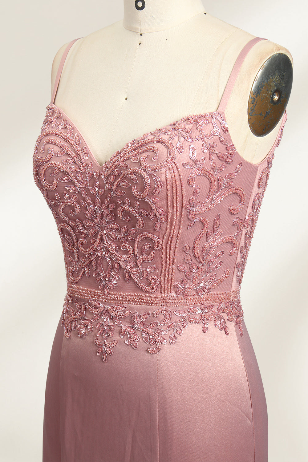 A photograph of a model mannequin wearing a floor-length, mauve satin gown with a deep V-neckline. The bodice is adorned with intricate lace detailing, featuring floral patterns and a subtle sheen. The gown has a thigh-high slit on the right side, adding a touch of elegance. The mannequin stands against a plain white background, highlighting the dress's smooth texture and elegant silhouette.04