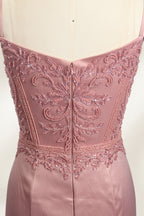 A photograph of a model mannequin wearing a floor-length, mauve satin gown with a deep V-neckline. The bodice is adorned with intricate lace detailing, featuring floral patterns and a subtle sheen. The gown has a thigh-high slit on the right side, adding a touch of elegance. The mannequin stands against a plain white background, highlighting the dress's smooth texture and elegant silhouette.05