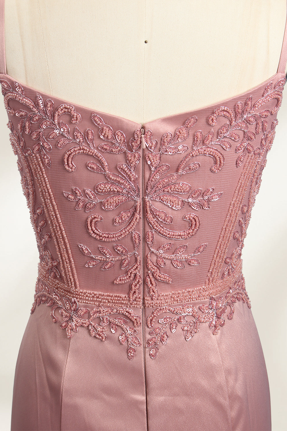 A photograph of a model mannequin wearing a floor-length, mauve satin gown with a deep V-neckline. The bodice is adorned with intricate lace detailing, featuring floral patterns and a subtle sheen. The gown has a thigh-high slit on the right side, adding a touch of elegance. The mannequin stands against a plain white background, highlighting the dress's smooth texture and elegant silhouette.05