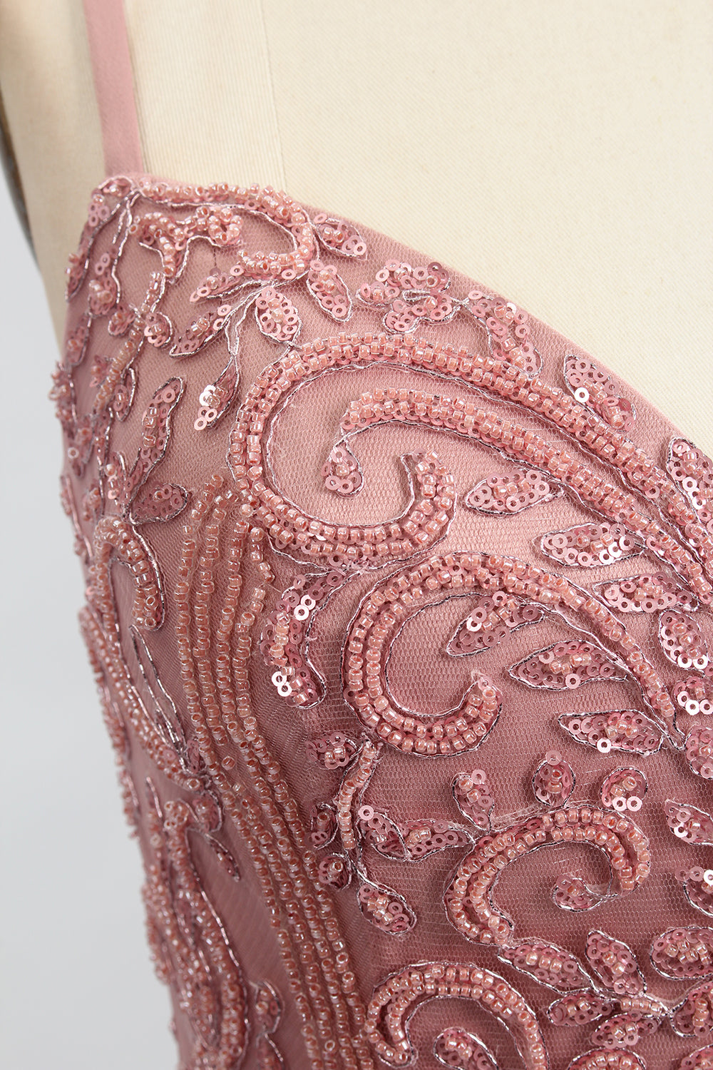 A photograph of a model mannequin wearing a floor-length, mauve satin gown with a deep V-neckline. The bodice is adorned with intricate lace detailing, featuring floral patterns and a subtle sheen. The gown has a thigh-high slit on the right side, adding a touch of elegance. The mannequin stands against a plain white background, highlighting the dress's smooth texture and elegant silhouette.0