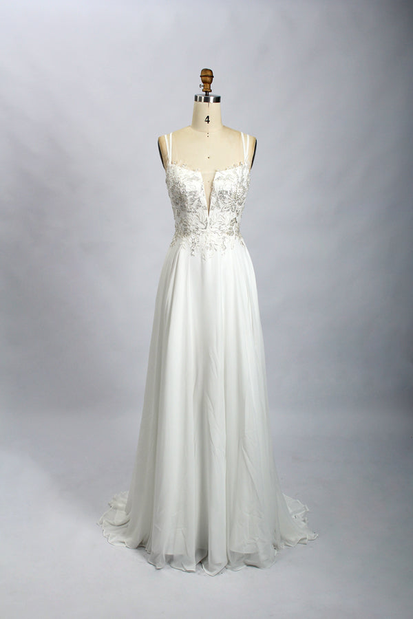 Photograph of a mannequin showcasing a floor-length, dark navy blue evening gown. The gown features a plunging V-neckline adorned with intricate beadwork and sequins. The fabric is a flowing chiffon, creating soft, elegant draping. The mannequin stands against a plain, light beige background, emphasizing the gown's luxurious texture and design. The mannequin's head is replaced with a wooden headpiece, and the dress is fitted to highlight the elegant, sophisticated style.08