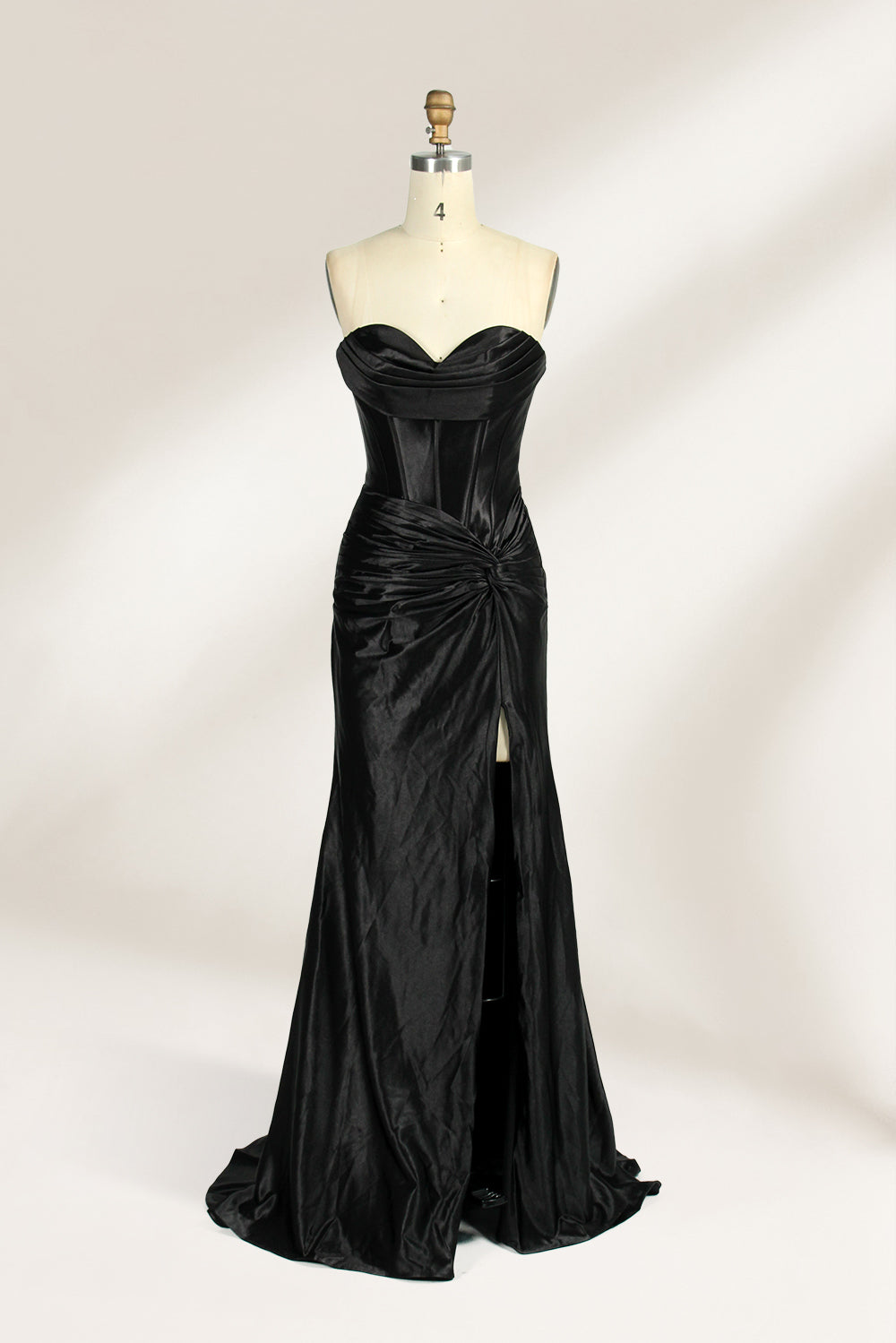 A mannequin showcases a strapless, blush - pink satin gown against a light backdrop. It features a ruched bodice with a draped neckline and a twisted detail at the waist, along with a mermaid silhouette and a side slit. The smooth satin fabric exudes elegance, perfect for formal events like galas.7