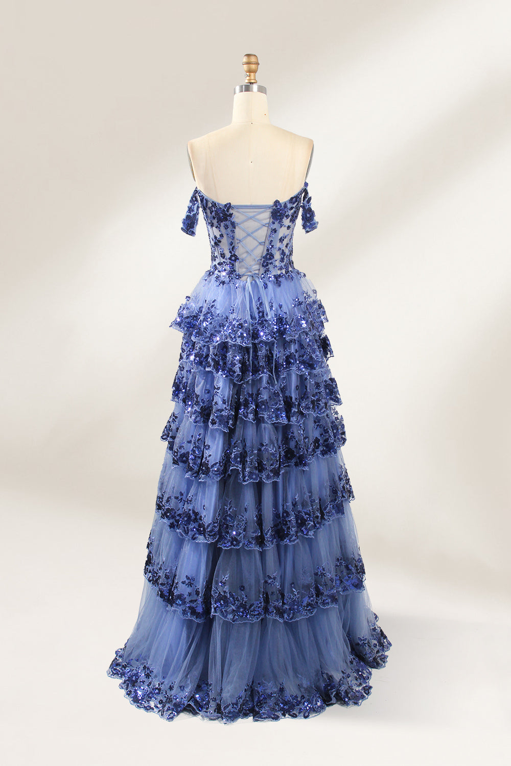 Photograph of a mannequin displaying a strapless, multi-layered, light blue tulle gown adorned with intricate floral embroidery. The gown has an off-shoulder neckline and a fitted bodice, cascading into voluminous, ruffled tiers. The background is plain white, highlighting the dress's delicate details. 5