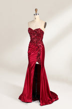 This photograph features a mannequin dressed in a strapless, floor-length, deep red satin evening gown. The gown is adorned with intricate sequin embroidery on the bodice and a high slit on the left side, revealing black stockings. The fabric has a smooth, luxurious texture. The mannequin stands on a black stool against a plain white background, creating a stark contrast that highlights the gown's vibrant color and detailed design. The overall style is elegant and glamorous, suitable for formal occasions.4