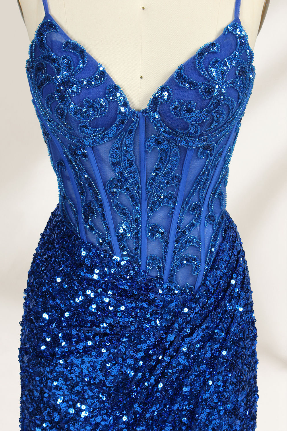 Set against a light background, a mannequin presents a blue gown adorned with sequins. It has thin straps, a deep V - neckline, and a mermaid - shaped skirt with a high side slit. The intricate sequin patterns and sheer bodice with embroidery add glamour, ideal for proms or formal dinners.7
