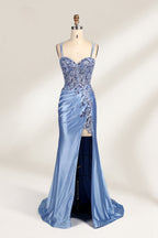 This photograph features a mannequin dressed in a luxurious, floor-length, light blue satin evening gown. The gown is intricately designed with delicate floral embroidery in silver and blue tones, primarily concentrated on the bodice and left hip. It has a plunging neckline and spaghetti straps, with a daring thigh-high slit on the left side. The mannequin is positioned against a plain, off-white background, allowing the gown's opulent texture and detailed craftsmanship to stand out. The gown exudes eleganc
