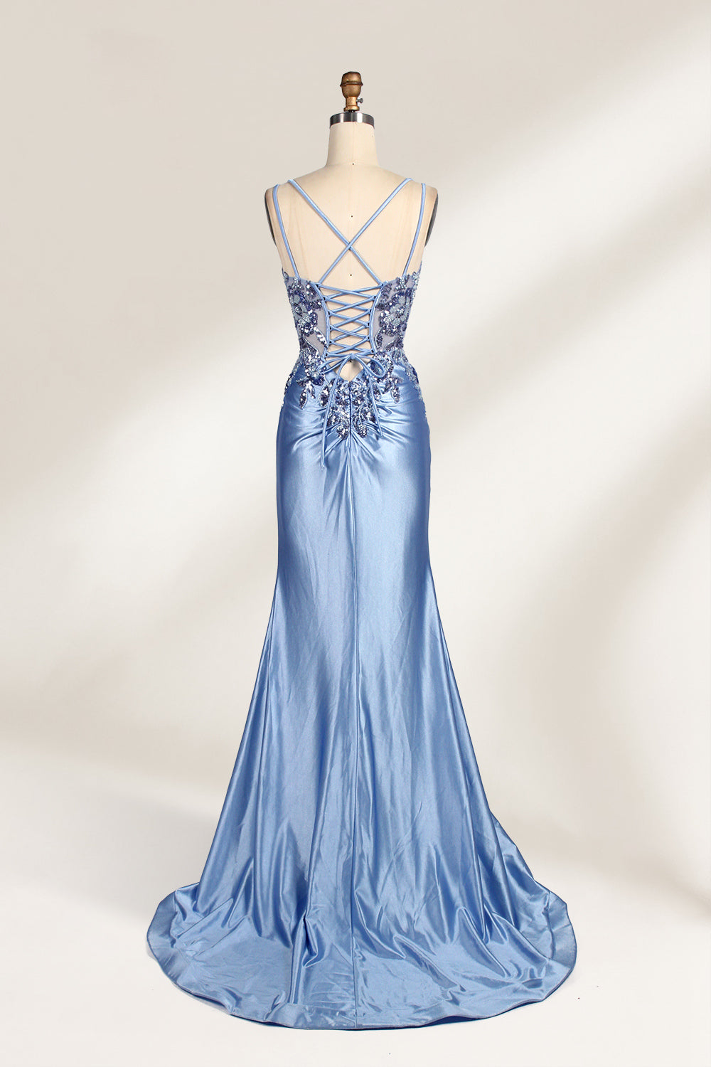 This photograph features a mannequin dressed in a luxurious, floor-length, light blue satin evening gown. The gown is intricately designed with delicate floral embroidery in silver and blue tones, primarily concentrated on the bodice and left hip. It has a plunging neckline and spaghetti straps, with a daring thigh-high slit on the left side. The mannequin is positioned against a plain, off-white background, allowing the gown's opulent texture and detailed craftsmanship to stand out. The gown exudes eleganc
