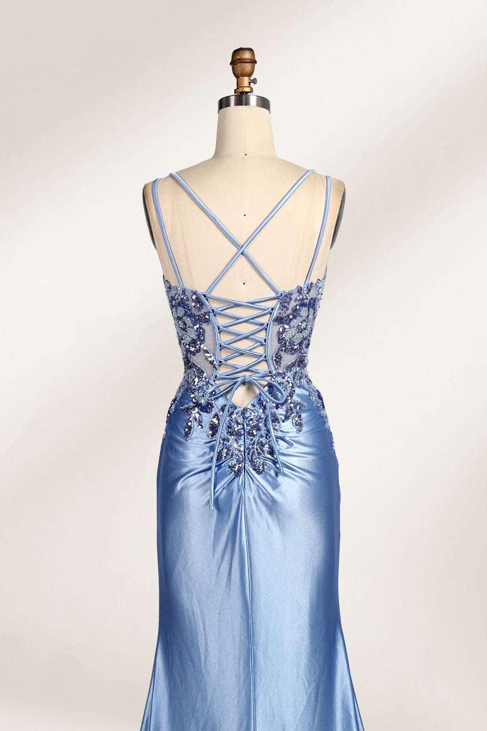 This photograph features a mannequin dressed in a luxurious, floor-length, light blue satin evening gown. The gown is intricately designed with delicate floral embroidery in silver and blue tones, primarily concentrated on the bodice and left hip. It has a plunging neckline and spaghetti straps, with a daring thigh-high slit on the left side. The mannequin is positioned against a plain, off-white background, allowing the gown's opulent texture and detailed craftsmanship to stand out. 5