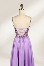 A photograph of a lavender, strapless, floor-length evening gown displayed on a dress form. The gown features intricate floral lace detailing on the bodice, transitioning into a flowing, chiffon skirt with a slight train. The dress form is positioned against a plain white background, emphasizing the gown's elegant and sophisticated design. The dress form has a wooden neck and shoulder structure with a small, round, black button at the top. The image captures the gown's luxurious texture and graceful .5