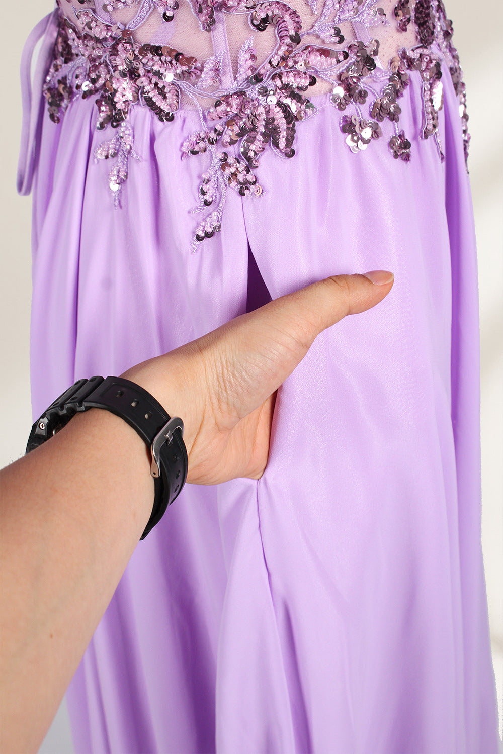 A photograph of a lavender, strapless, floor-length evening gown displayed on a dress form. The gown features intricate floral lace detailing on the bodice, transitioning into a flowing, chiffon skirt with a slight train. The dress form is positioned against a plain white background, emphasizing the gown's elegant and sophisticated design. The dress form has a wooden neck and shoulder structure with a small, round, black button at the top. The image captures the gown's luxurious texture and graceful .6