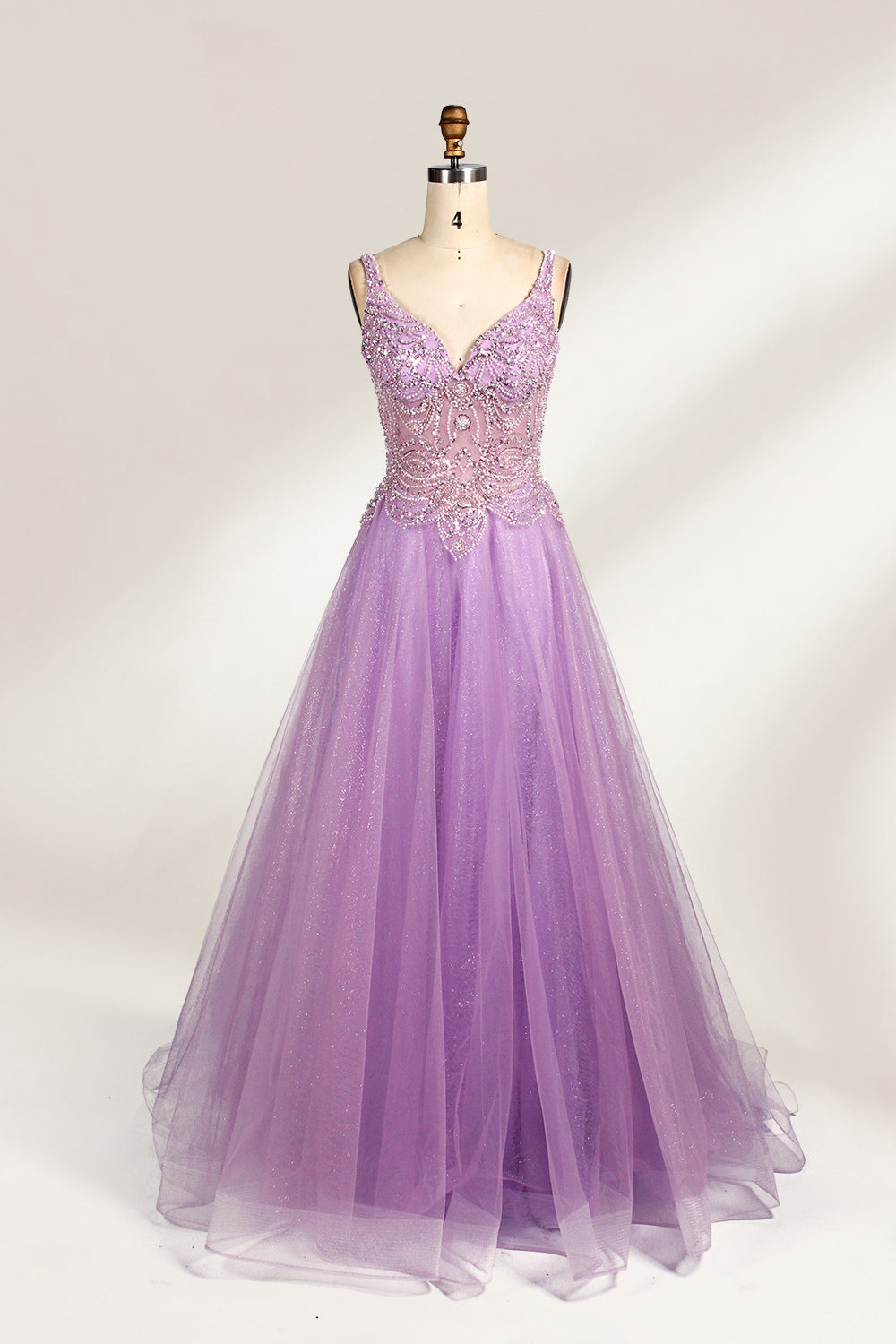 A mannequin showcases a lavender - purple tulle gown. It has a V - neck, beaded bodice, and a voluminous skirt. The elegant design, with intricate beadwork, suits formal events like galas or proms, radiating charm and grace.1