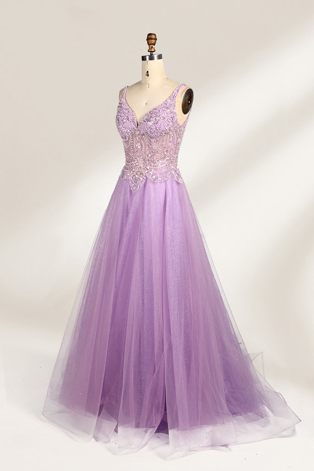 A mannequin showcases a lavender - purple tulle gown. It has a V - neck, beaded bodice, and a voluminous skirt. The elegant design, with intricate beadwork, suits formal events like galas or proms, radiating charm and grace.5