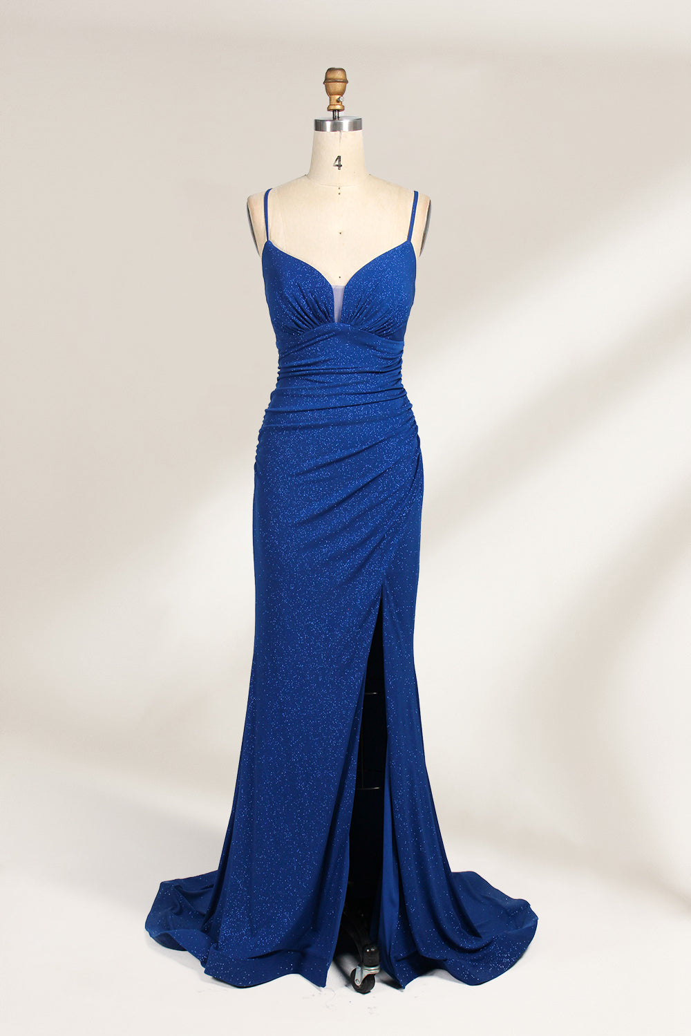 A mannequin showcases a royal - blue, glittery gown. It has thin straps, a ruched bodice, and a high side slit with a subtle train. The elegant design, with shimmering fabric, suits formal events like galas or proms, radiating sophistication.1