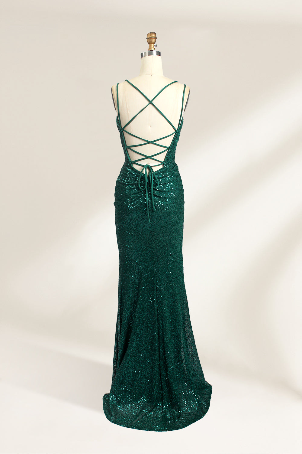 Photograph of a mannequin wearing a floor-length, deep green sequin dress with a plunging V-neckline, spaghetti straps, and a daring thigh-high slit on the left side. The dress has a fitted bodice and a flowing, slightly flared skirt. The mannequin is displayed against a plain white background with soft, diffused lighting creating gentle shadows.05