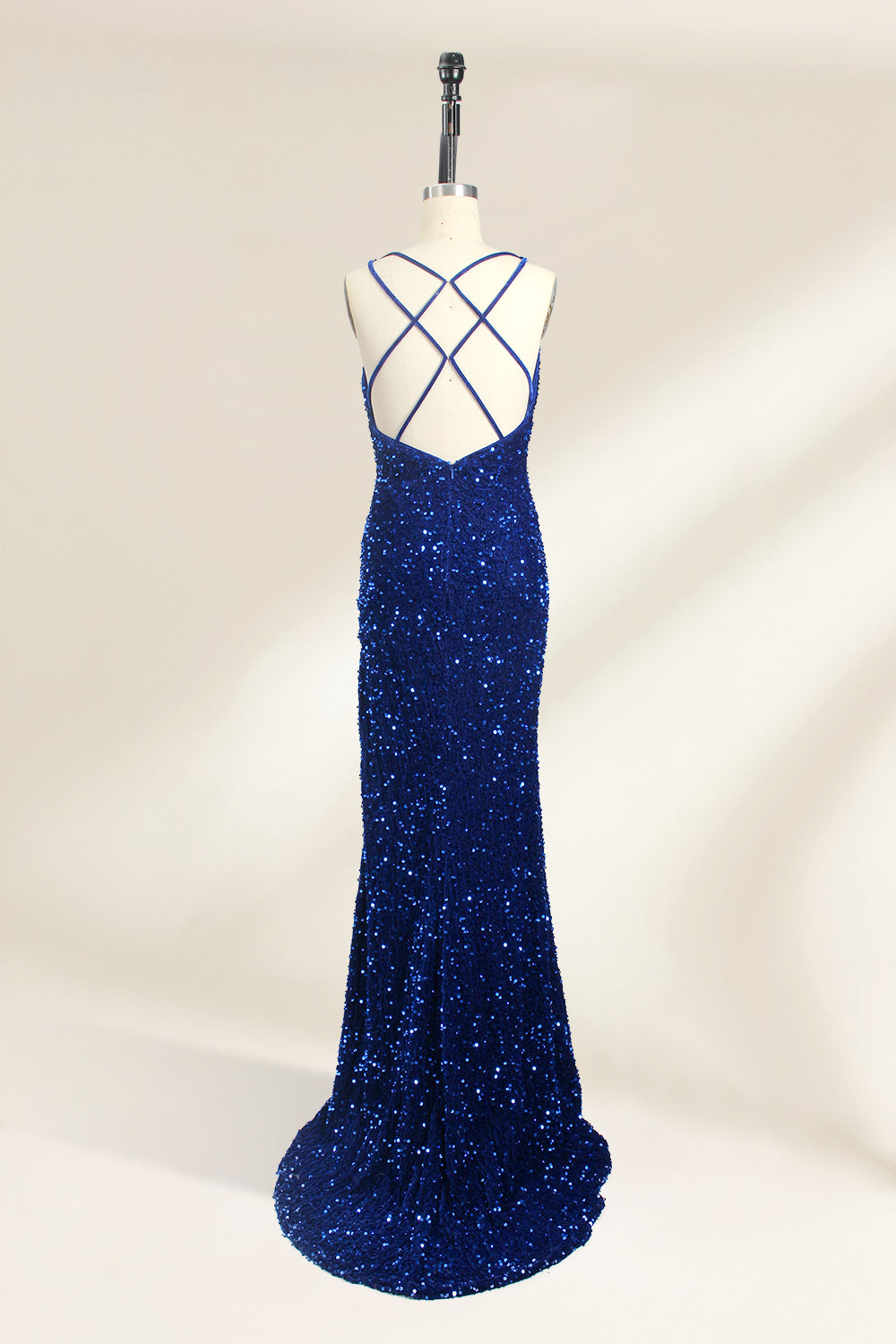 Photograph of a mannequin wearing a floor-length, deep V-neck, navy blue sequin dress with a high slit on the right side. The dress has a fitted bodice and a flared skirt. The background is a plain, light beige. The mannequin stands on a white pedestal, and the dress sparkles under soft, diffused lighting.02