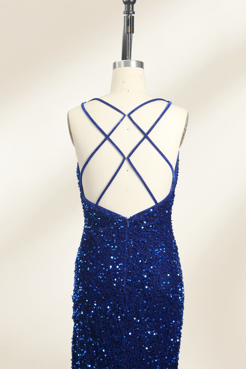 Photograph of a mannequin wearing a floor-length, deep V-neck, navy blue sequin dress with a high slit on the right side. The dress has a fitted bodice and a flared skirt. The background is a plain, light beige. The mannequin stands on a white pedestal, and the dress sparkles under soft, diffused lighting.05