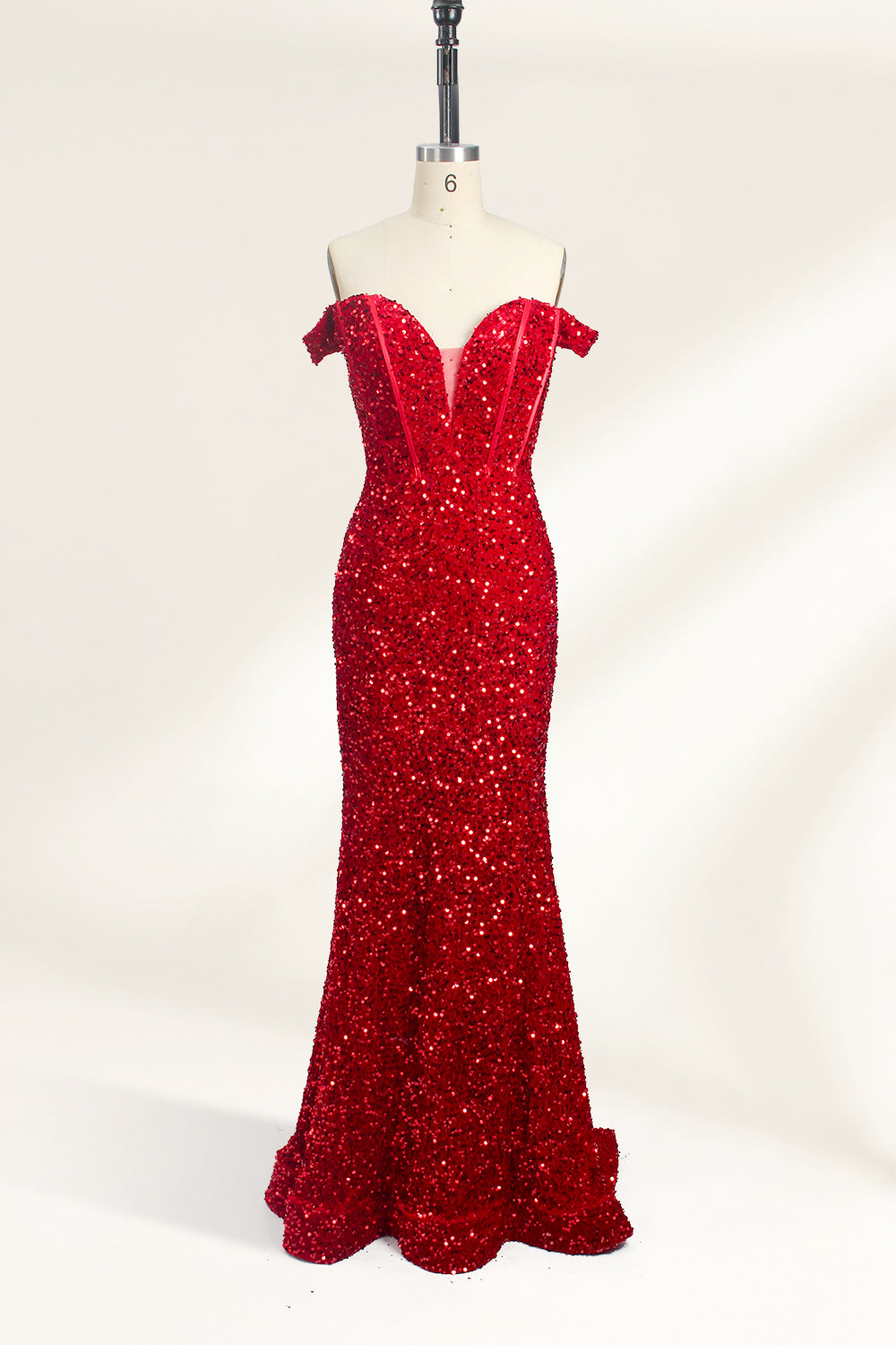 A photograph of a mannequin showcasing an off-the-shoulder, floor-length red sequin gown with a plunging V-neckline. The dress has a fitted bodice and a flared skirt, creating a glamorous, elegant appearance. The mannequin stands against a plain white background, emphasizing the dress's vibrant color and intricate details.01