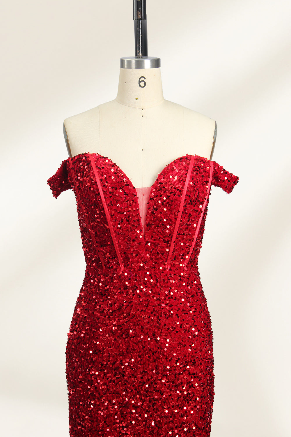 A photograph of a mannequin showcasing an off-the-shoulder, floor-length red sequin gown with a plunging V-neckline. The dress has a fitted bodice and a flared skirt, creating a glamorous, elegant appearance. The mannequin stands against a plain white background, emphasizing the dress's vibrant color and intricate details.04