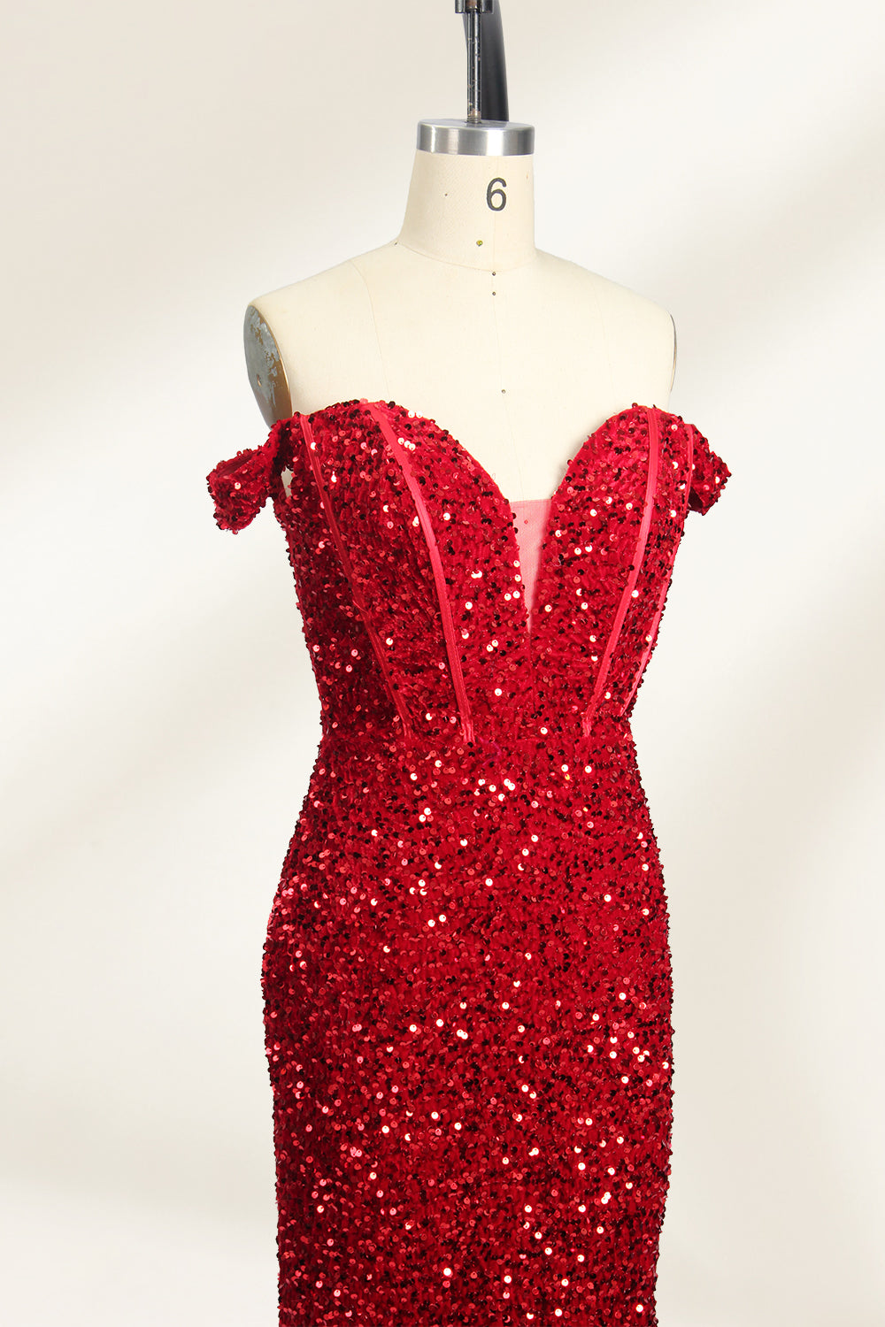 A photograph of a mannequin showcasing an off-the-shoulder, floor-length red sequin gown with a plunging V-neckline. The dress has a fitted bodice and a flared skirt, creating a glamorous, elegant appearance. The mannequin stands against a plain white background, emphasizing the dress's vibrant color and intricate details.04