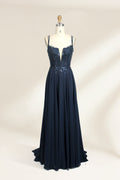 Photograph of a mannequin showcasing a floor-length, dark navy blue evening gown. The gown features a plunging V-neckline adorned with intricate beadwork and sequins. The fabric is a flowing chiffon, creating soft, elegant draping. The mannequin stands against a plain, light beige background, emphasizing the gown's luxurious texture and design. The mannequin's head is replaced with a wooden headpiece, and the dress is fitted to highlight the elegant, sophisticated style.01