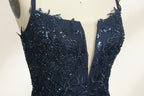 Photograph of a mannequin showcasing a floor-length, dark navy blue evening gown. The gown features a plunging V-neckline adorned with intricate beadwork and sequins. The fabric is a flowing chiffon, creating soft, elegant draping. The mannequin stands against a plain, light beige background, emphasizing the gown's luxurious texture and design. The mannequin's head is replaced with a wooden headpiece, and the dress is fitted to highlight the elegant, sophisticated style.06