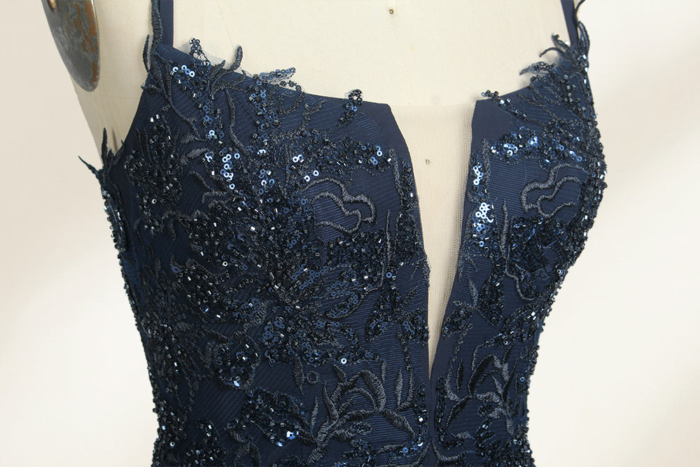 Photograph of a mannequin showcasing a floor-length, dark navy blue evening gown. The gown features a plunging V-neckline adorned with intricate beadwork and sequins. The fabric is a flowing chiffon, creating soft, elegant draping. The mannequin stands against a plain, light beige background, emphasizing the gown's luxurious texture and design. The mannequin's head is replaced with a wooden headpiece, and the dress is fitted to highlight the elegant, sophisticated style.06