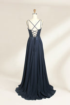 Photograph of a mannequin showcasing a floor-length, dark navy blue evening gown. The gown features a plunging V-neckline adorned with intricate beadwork and sequins. The fabric is a flowing chiffon, creating soft, elegant draping. The mannequin stands against a plain, light beige background, emphasizing the gown's luxurious texture and design. The mannequin's head is replaced with a wooden headpiece, and the dress is fitted to highlight the elegant, sophisticated style.02