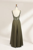 Photograph of an elegant, sleeveless, floor-length gown displayed on a dress form. The gown is a rich olive green with a fitted bodice adorned with intricate, sparkling embellishments. The neckline is a deep V, and the waistline is subtly cinched. The dress flows into a soft, gathered skirt. The background is a plain, light beige, enhancing the gown's luxurious texture and shimmering details.02