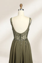 Photograph of an elegant, sleeveless, floor-length gown displayed on a dress form. The gown is a rich olive green with a fitted bodice adorned with intricate, sparkling embellishments. The neckline is a deep V, and the waistline is subtly cinched. The dress flows into a soft, gathered skirt. The background is a plain, light beige, enhancing the gown's luxurious texture and shimmering details.06