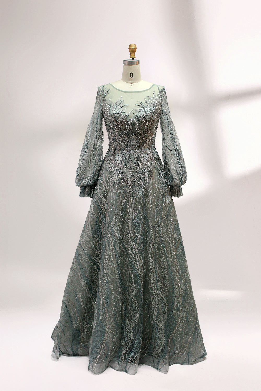 Presented on a mannequin is a deep - red evening gown. It features a sheer neckline, long billowy sleeves, and intricate gold - toned embroidery throughout. The elaborate design gives off a luxurious and elegant vibe, ideal for formal occasions.2