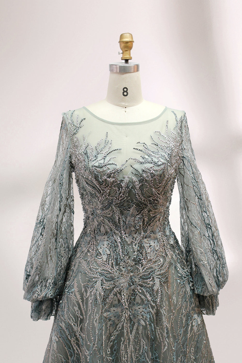 Presented on a mannequin is a deep - red evening gown. It features a sheer neckline, long billowy sleeves, and intricate gold - toned embroidery throughout. The elaborate design gives off a luxurious and elegant vibe, ideal for formal occasions.4