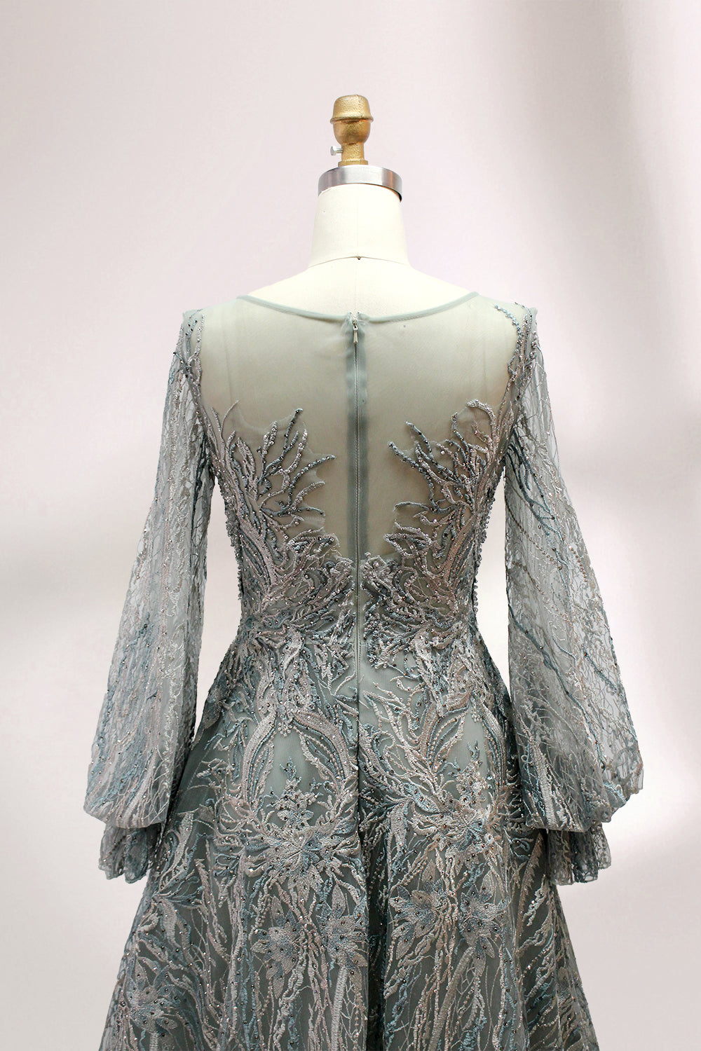 Presented on a mannequin is a deep - red evening gown. It features a sheer neckline, long billowy sleeves, and intricate gold - toned embroidery throughout. The elaborate design gives off a luxurious and elegant vibe, ideal for formal occasions.5