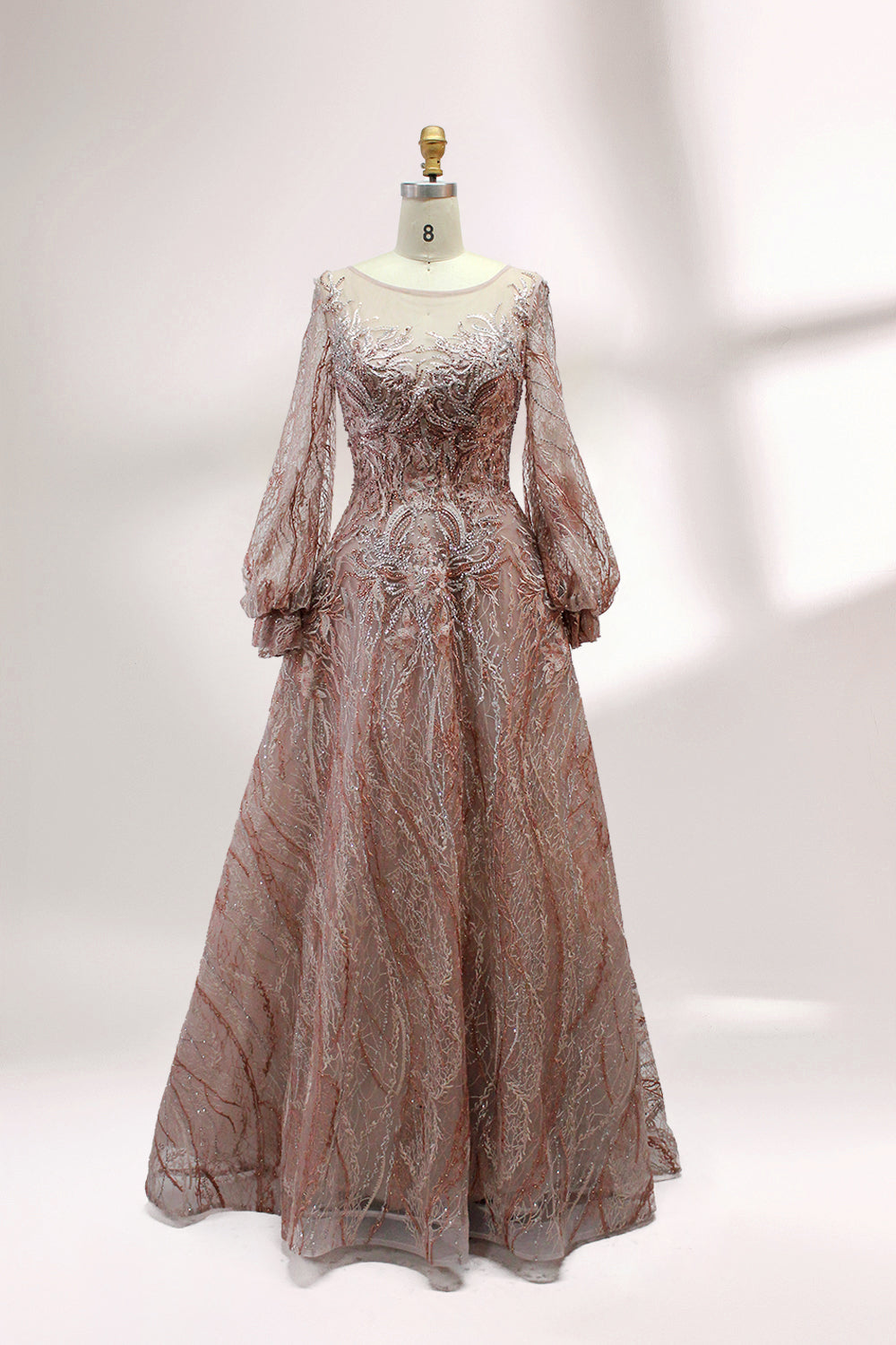 Presented on a mannequin is a deep - red evening gown. It features a sheer neckline, long billowy sleeves, and intricate gold - toned embroidery throughout. The elaborate design gives off a luxurious and elegant vibe, ideal for formal occasions.3