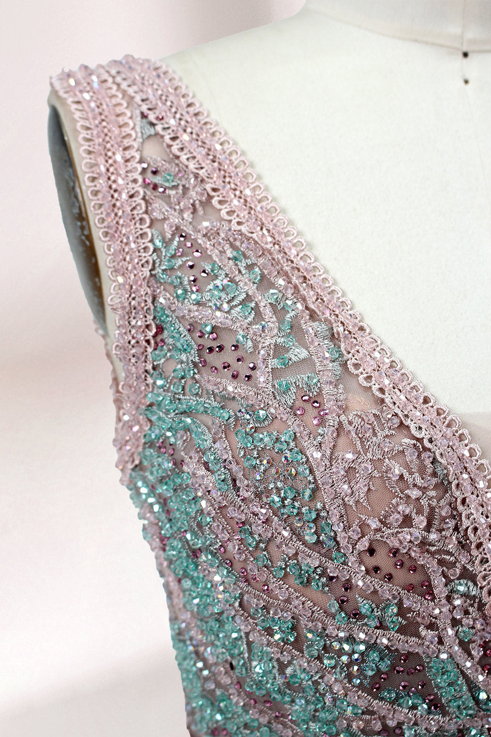 Displayed on a mannequin is a pink - hued evening gown. It features a deep V - neckline, intricate floral embroidery in shades of blue and pink, and a flowing skirt. The elegant design creates a romantic and sophisticated look, perfect for formal events.6