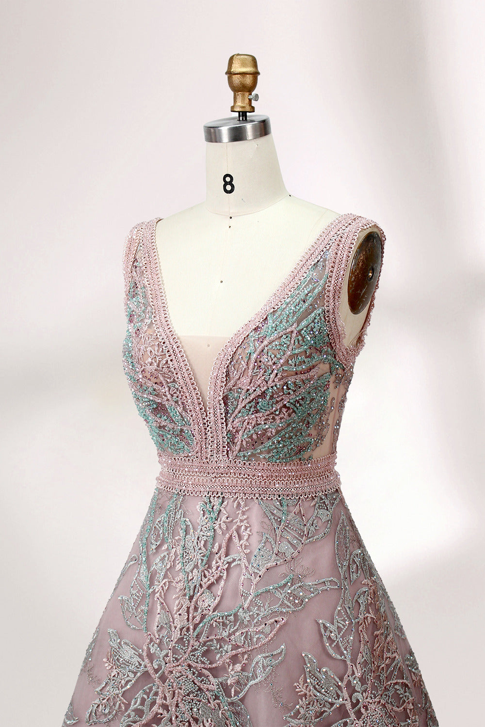 Displayed on a mannequin is a pink - hued evening gown. It features a deep V - neckline, intricate floral embroidery in shades of blue and pink, and a flowing skirt. The elegant design creates a romantic and sophisticated look, perfect for formal events.4