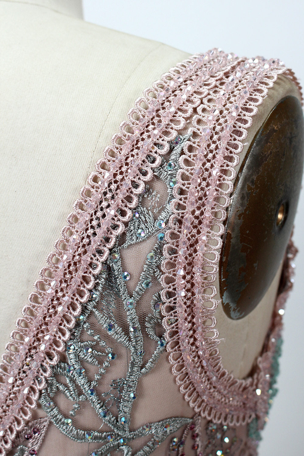 Displayed on a mannequin is a pink - hued evening gown. It features a deep V - neckline, intricate floral embroidery in shades of blue and pink, and a flowing skirt. The elegant design creates a romantic and sophisticated look, perfect for formal events.7