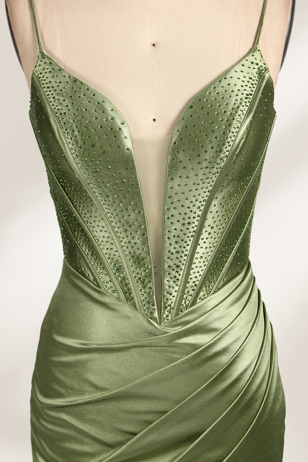 A mannequin showcases an olive - green satin gown. It has thin straps, a deep V - neck, ruched bodice, and a high side slit with sheer details. The elegant design, blending satin and intricate ruching, suits formal events like galas or proms, radiating sophistication.3
