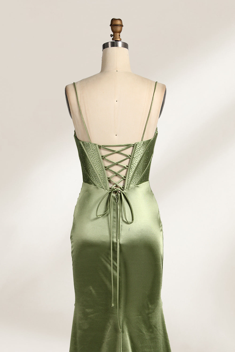 A mannequin showcases an olive - green satin gown. It has thin straps, a deep V - neck, ruched bodice, and a high side slit with sheer details. The elegant design, blending satin and intricate ruching, suits formal events like galas or proms, radiating sophistication.2