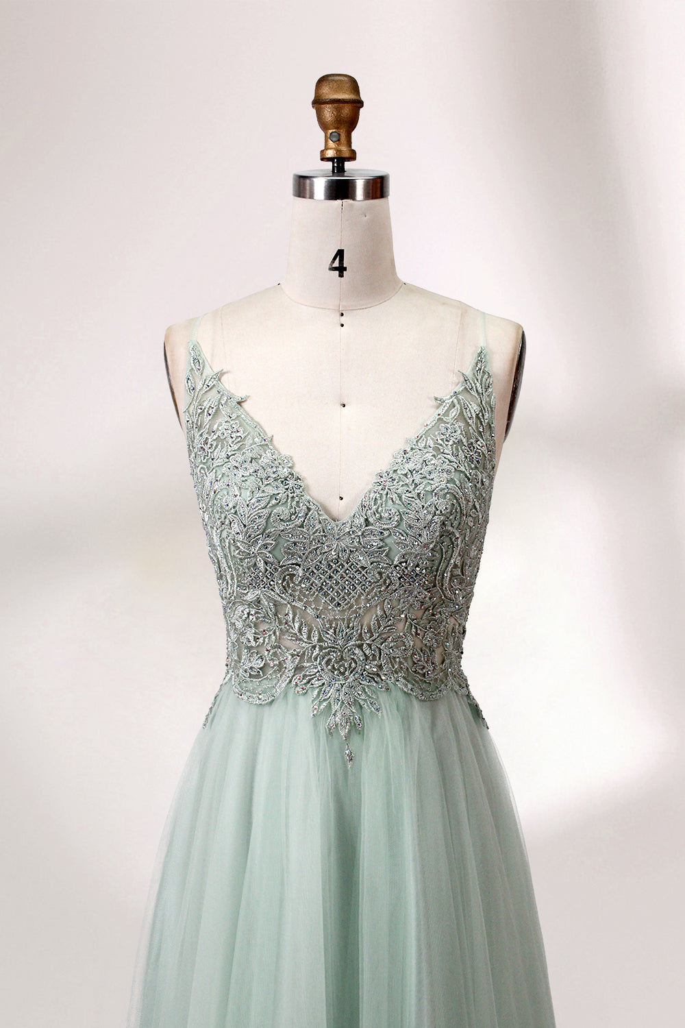 A mannequin showcases a light - green tulle gown with a lace - embroidered, sheer bodice. It has thin straps, a deep V - neckline, and a voluminous skirt. The delicate lace and flowing tulle create a romantic look, perfect for formal events like weddings or proms, exuding elegance.
4