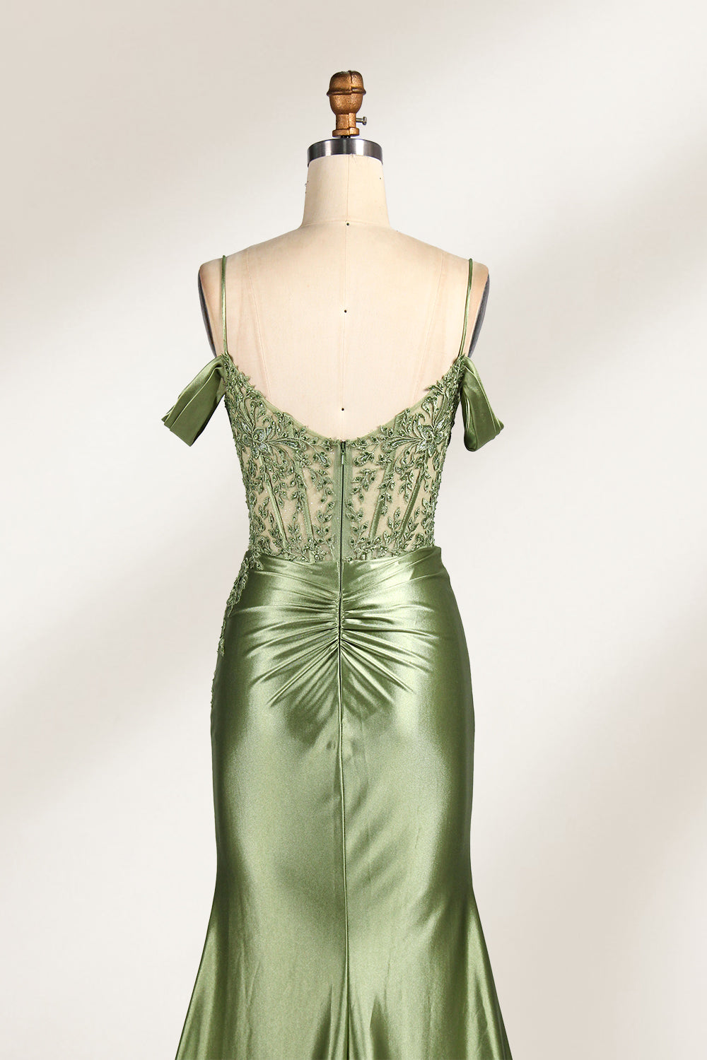 A mannequin displays a rose - gold satin gown. It has thin straps, off - shoulder lace - detailed sleeves, a ruched bodice, and a high side slit. The elegant design, blending satin and lace, suits formal events like galas or weddings.6