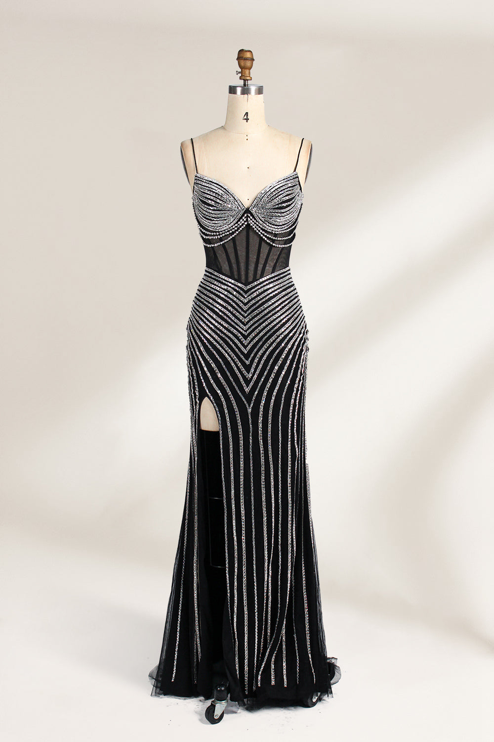 A mannequin showcases a black gown with silver beading. It has thin straps, a sheer bodice, and a high side slit. The geometric beading pattern adds glamour, making it perfect for formal events like galas or proms, radiating sophistication.1