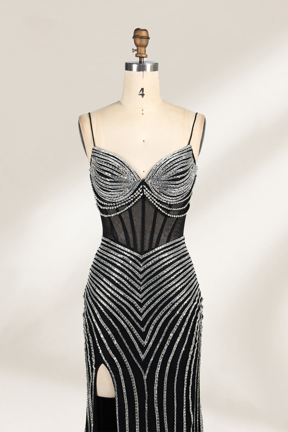 A mannequin showcases a black gown with silver beading. It has thin straps, a sheer bodice, and a high side slit. The geometric beading pattern adds glamour, making it perfect for formal events like galas or proms, radiating sophistication.3