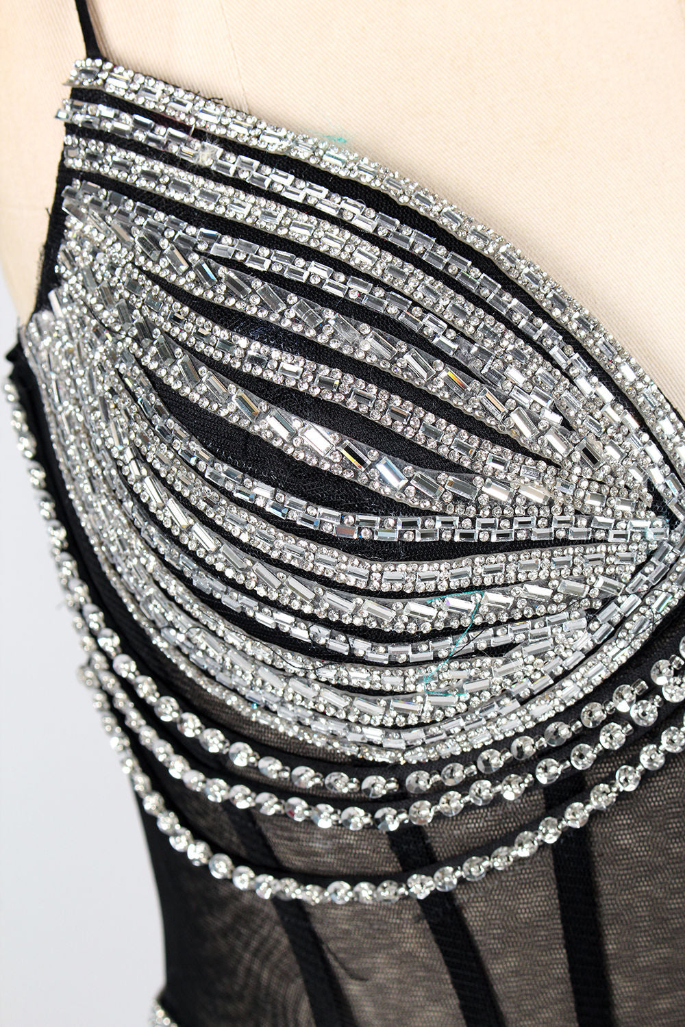 A mannequin showcases a black gown with silver beading. It has thin straps, a sheer bodice, and a high side slit. The geometric beading pattern adds glamour, making it perfect for formal events like galas or proms, radiating sophistication.5
