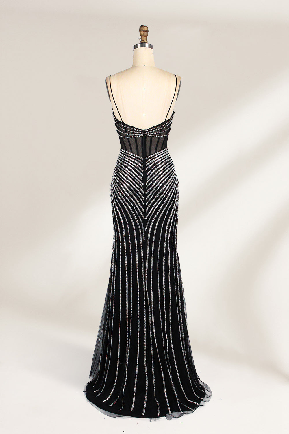 A mannequin showcases a black gown with silver beading. It has thin straps, a sheer bodice, and a high side slit. The geometric beading pattern adds glamour, making it perfect for formal events like galas or proms, radiating sophistication.2